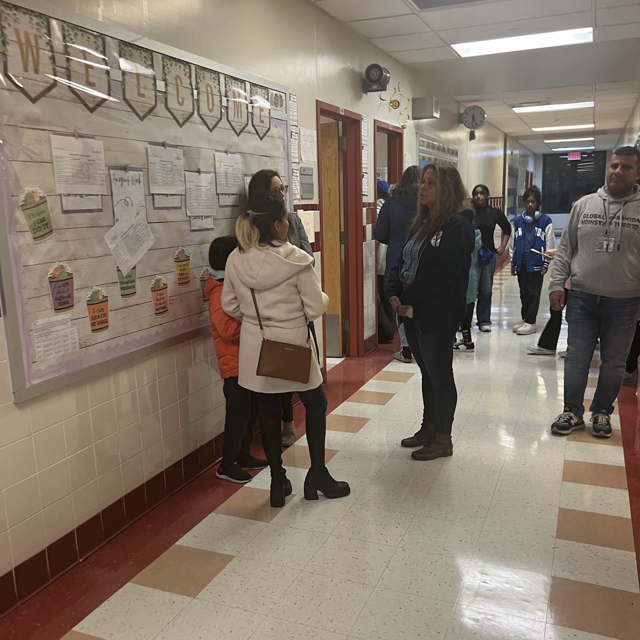Families and students look at a bulletin board display in a school hallway.