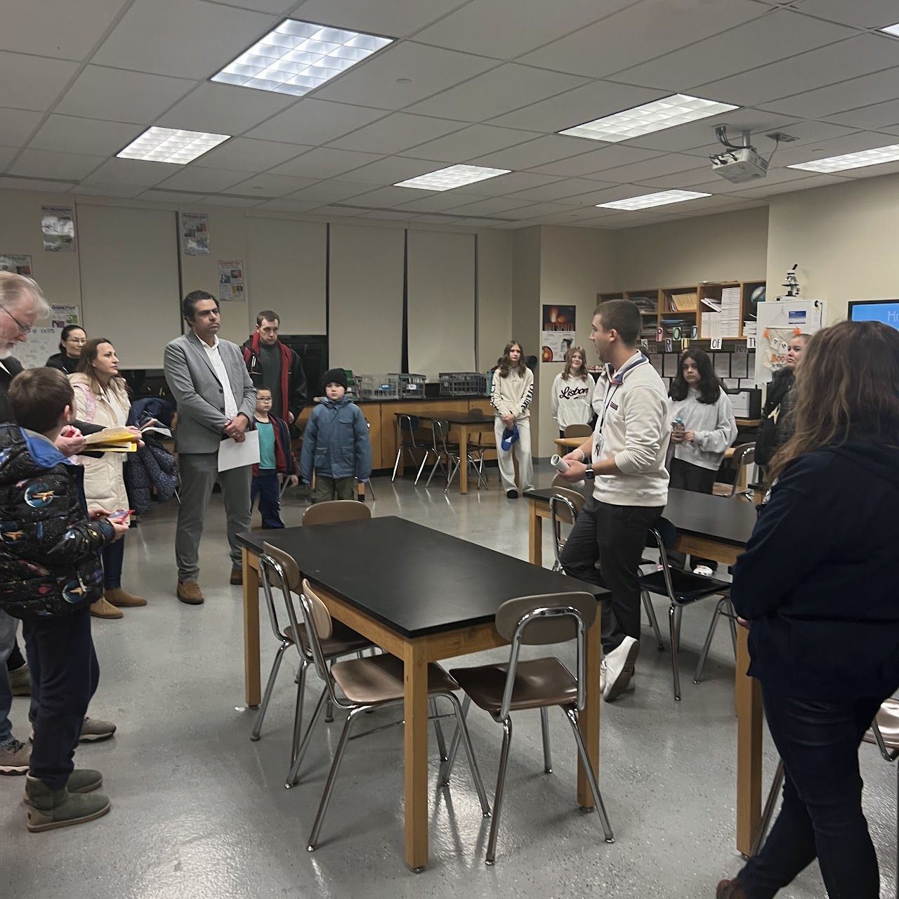 Families gather in a science classroom with black lab tables during the presentation.