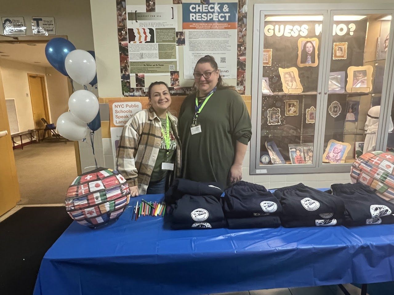 Two staff members stand behind a table of navy school sweatshirts decorated with balloons.