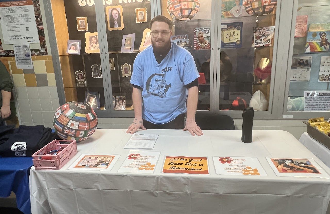 A staff member in a light blue shirt stands at a table of program flyers.
